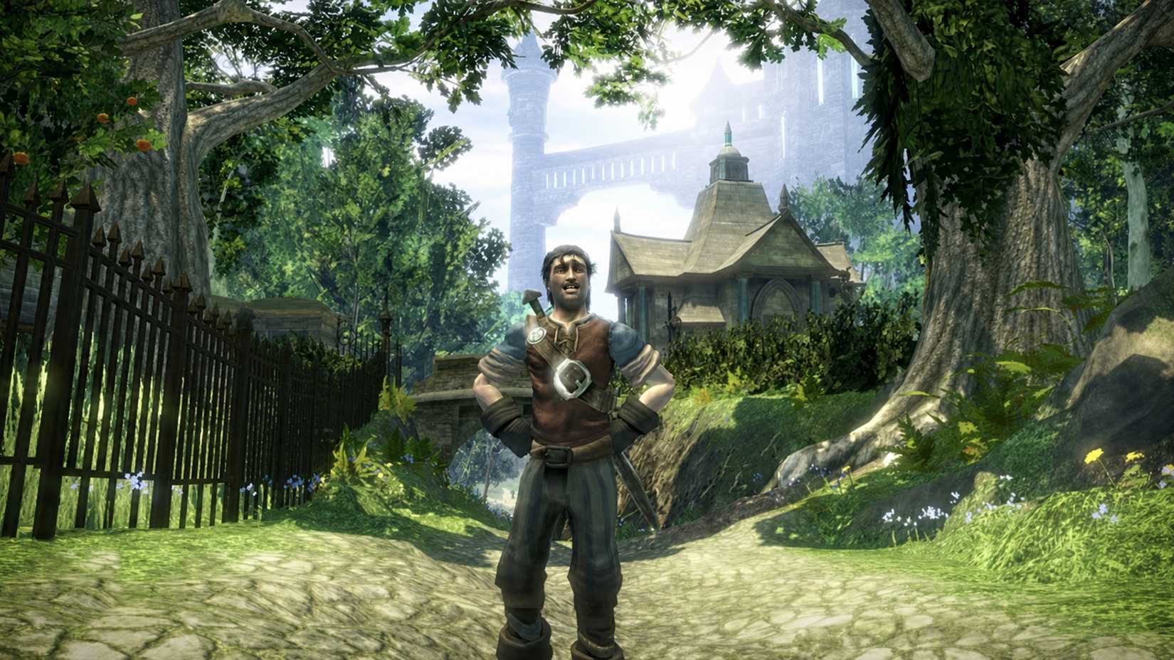 The male Hero in Fable 2 stands with his hands on his hips on a sunlit cobblestone path, surrounded by lush trees and an iron fence, with a stone chapel and towering castle in the background