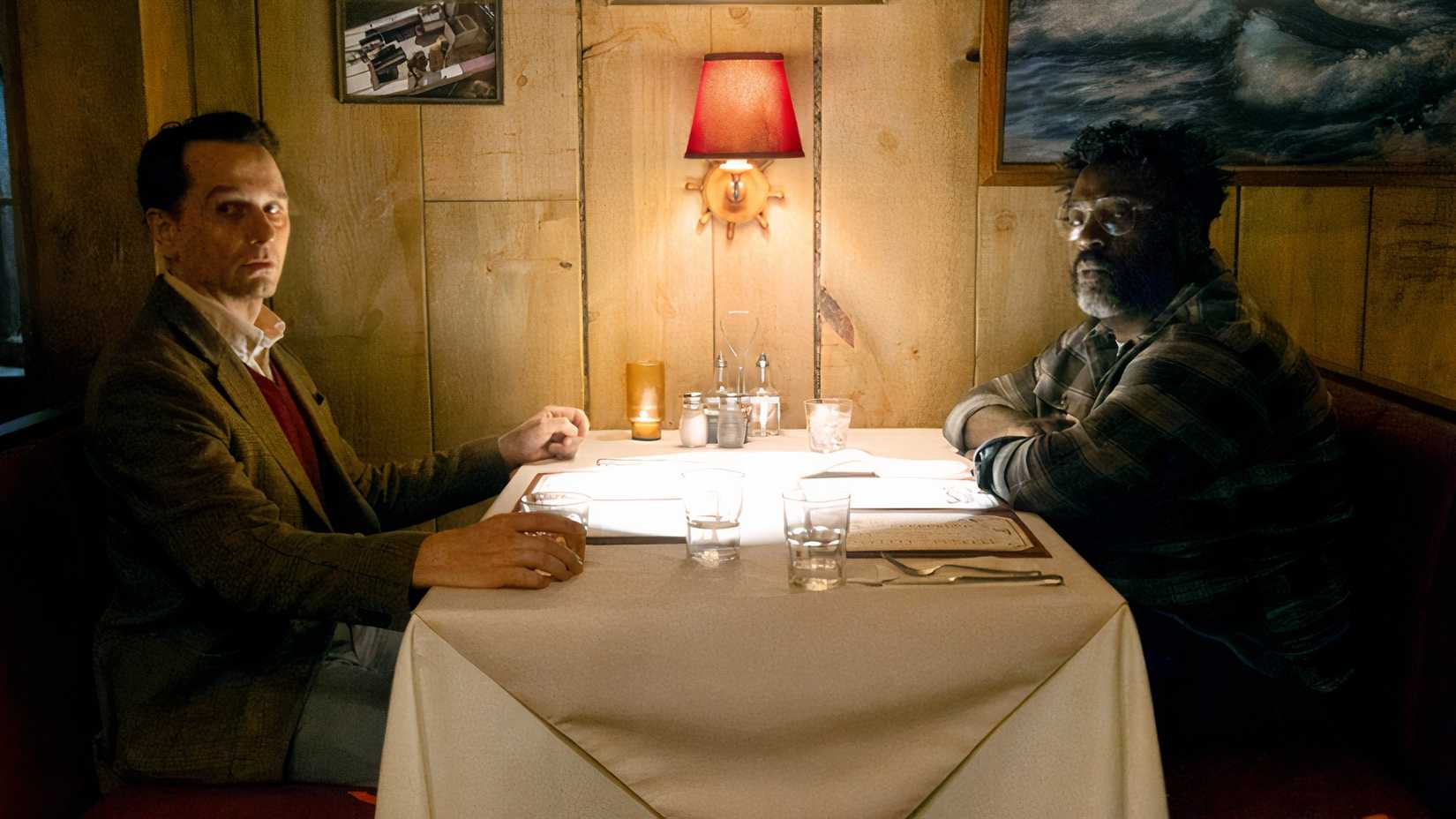 Matthew Rhys as Mayor Tom Loftis sitting across from Bashir Salahuddin as Travel Writer Arthur Lloyd in booth at the Salty Whale