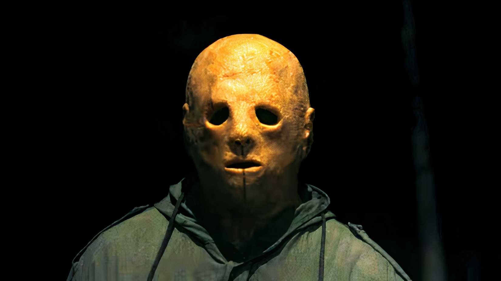 a creepily lit close up of the Boogeyman killer wearing a green hooded jacket and a deeply aged mask in Widow's Bay