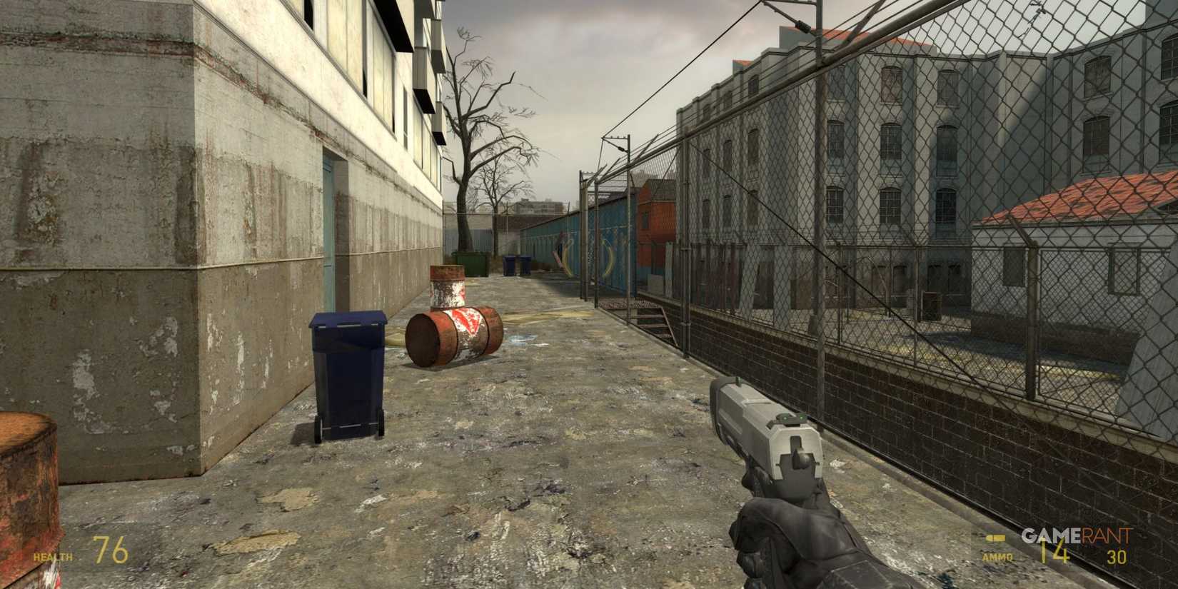Urban outdoor area with barrels and fences, player holding a pistol in Half-Life 2