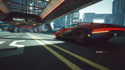 A wide-angle view of a futuristic red sports car driving across a Night City bridge in Cyberpunk 2077.